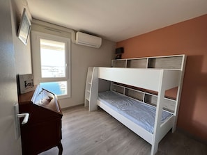 Quarto com cama de solteiro e beliche, escrivaninha, cadeira, janela com vista e ar condicionado.