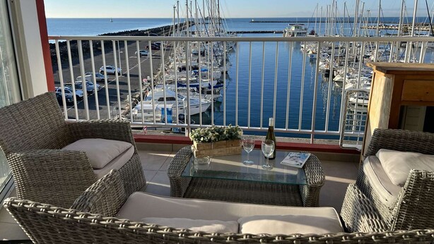A balcony with wicker furniture, a glass table, and a view of a marina with boats.