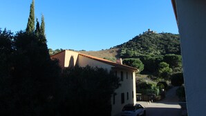 Un edificio con techo de tejas rojas, rodeado de vegetación y una colina con una estructura similar a un castillo al fondo.