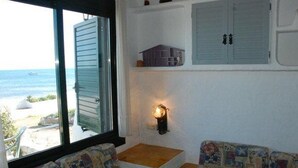 Une chambre avec vue sur la plage, une fenêtre avec des volets, une petite table et un canapé aux motifs colorés.