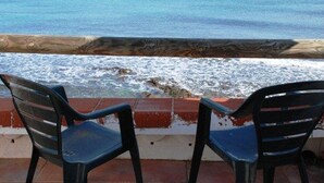 Deux chaises en plastique noir sont placées face à une rambarde en bois, d’où l’on a vue sur l’océan.