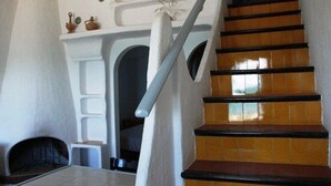 Un escalier avec des marches en bois et une rampe blanche, menant à une pièce dotée d’une cheminée blanche et d’une petite étagère ornée d’objets décoratifs.