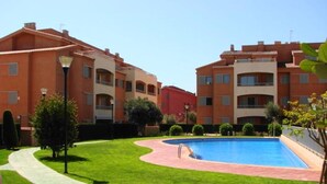 A residential building with a swimming pool, surrounded by well-maintained grass and a paved walkway.