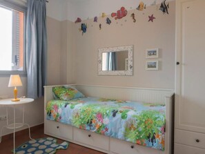 A bedroom with a bed, a small bedside table, a lamp, a mirror, and wall decorations.