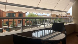 A balcony with a table and chairs, a view of neighboring buildings, and a large awning providing shade.
