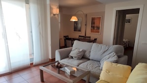 A living room with a sofa, a yellow armchair, a glass coffee table, and a dining area in the background. - Magnificent Duplex with Pool in L'Ametlla de Mar (L'Ametlla de Mar)