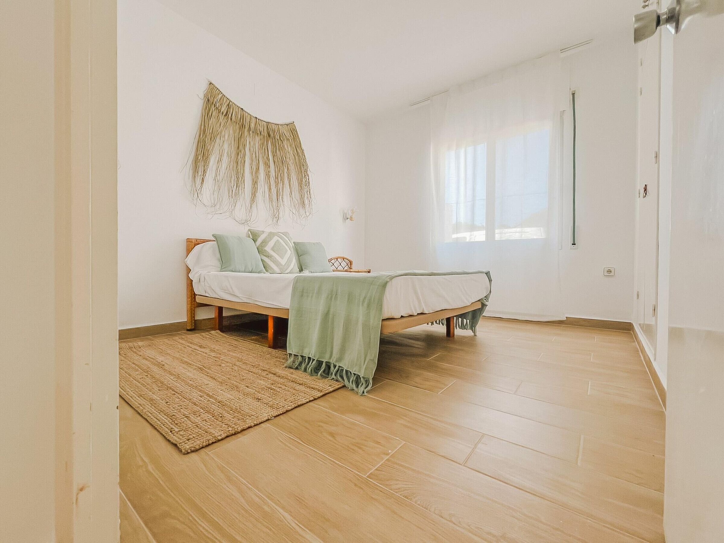 A bedroom with a bed, a woven rug, and a wall hanging.