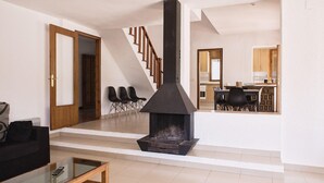 A modern living room with a glass coffee table, a fireplace, and a staircase leading to a kitchen area. - Coastal Villa with Private Pool, Steps from Beach, 4 Bedrooms, BBQ, Wi-Fi, Family-Friendly (L'Ametlla de Mar)