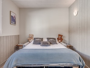 Une chambre à coucher avec un lit, deux tables de chevet, deux ours en peluche et un tableau encadré au mur.