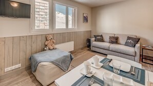 A cozy room with a sofa, a dining table set for two, a teddy bear, and a TV mounted on the wall. - PREMIUM Studio in Tignes, 2 people, WIFI included (Tignes)