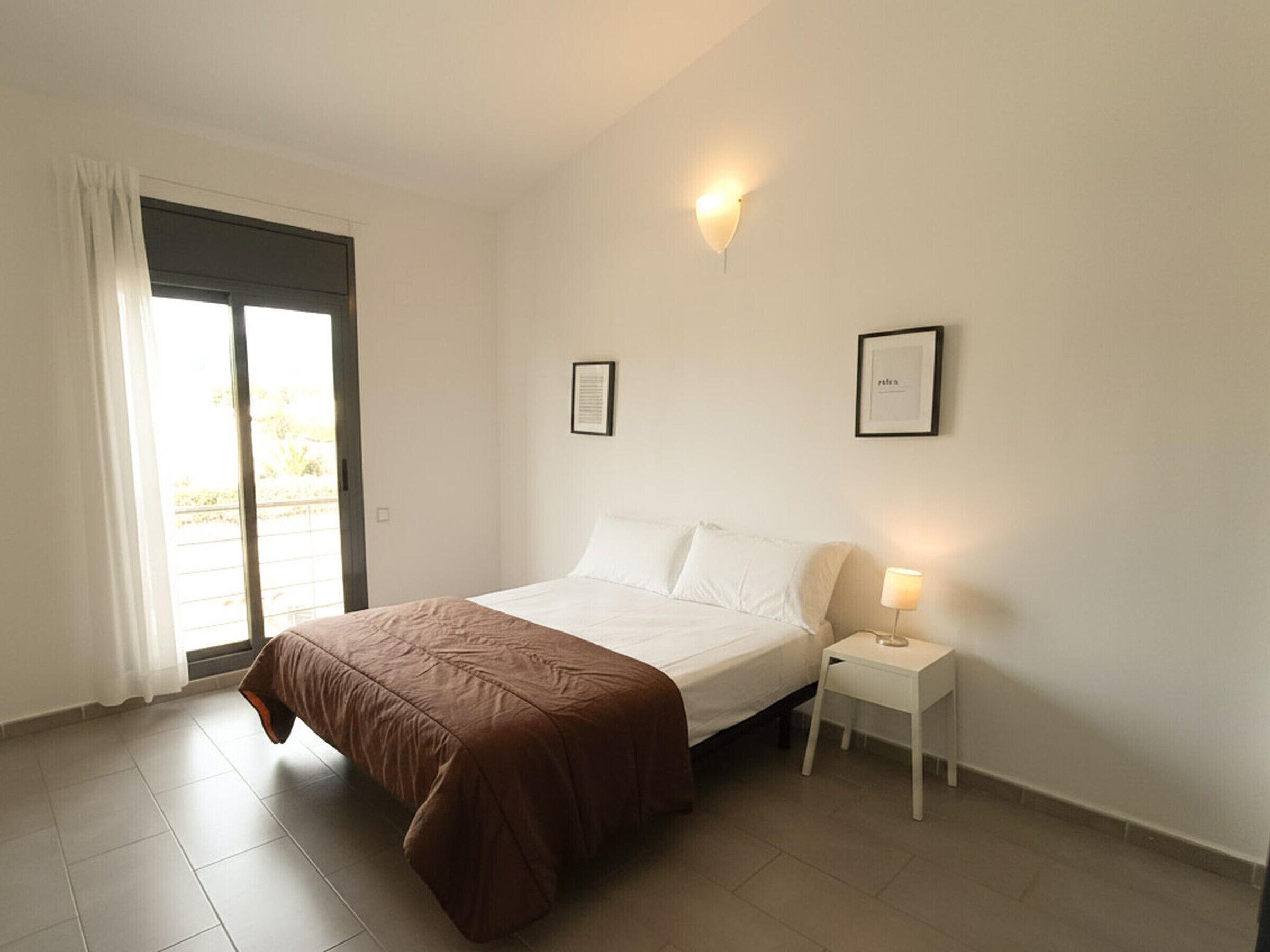 A hotel room with a bed, a nightstand, a wall-mounted light, and a door leading to a balcony.
