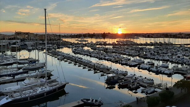 A marina with numerous boats docked, a clear sky, and the sun setting in the background. - 1BR with AC, Pool, Private Garage (Cap d'Agde)