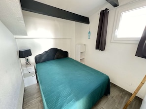 Quarto com cama, mesa de cabeceira, luminária, armário e janela com cortinas.
