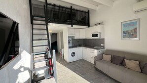A compact living space with a kitchenette, a sofa, and a staircase leading to an upper level. - 1BR with AC, Pool, Private Garage (Cap d'Agde)