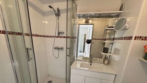 A modern bathroom with a glass-enclosed shower, a vanity with a mirror, and a tiled backsplash. - 1BR with AC, Pool, Private Garage (Cap d'Agde)