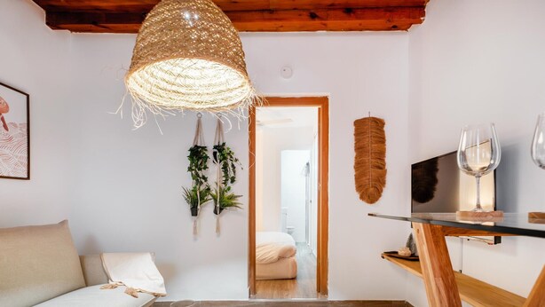 Un accogliente soggiorno con soffitto in legno, lampada intrecciata, divano, tavolino rotondo in legno e TV su un mobiletto in legno.