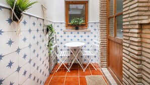 Un piccolo patio con tavolo e sedie bianche, una pianta in vaso e una finestra con vista.