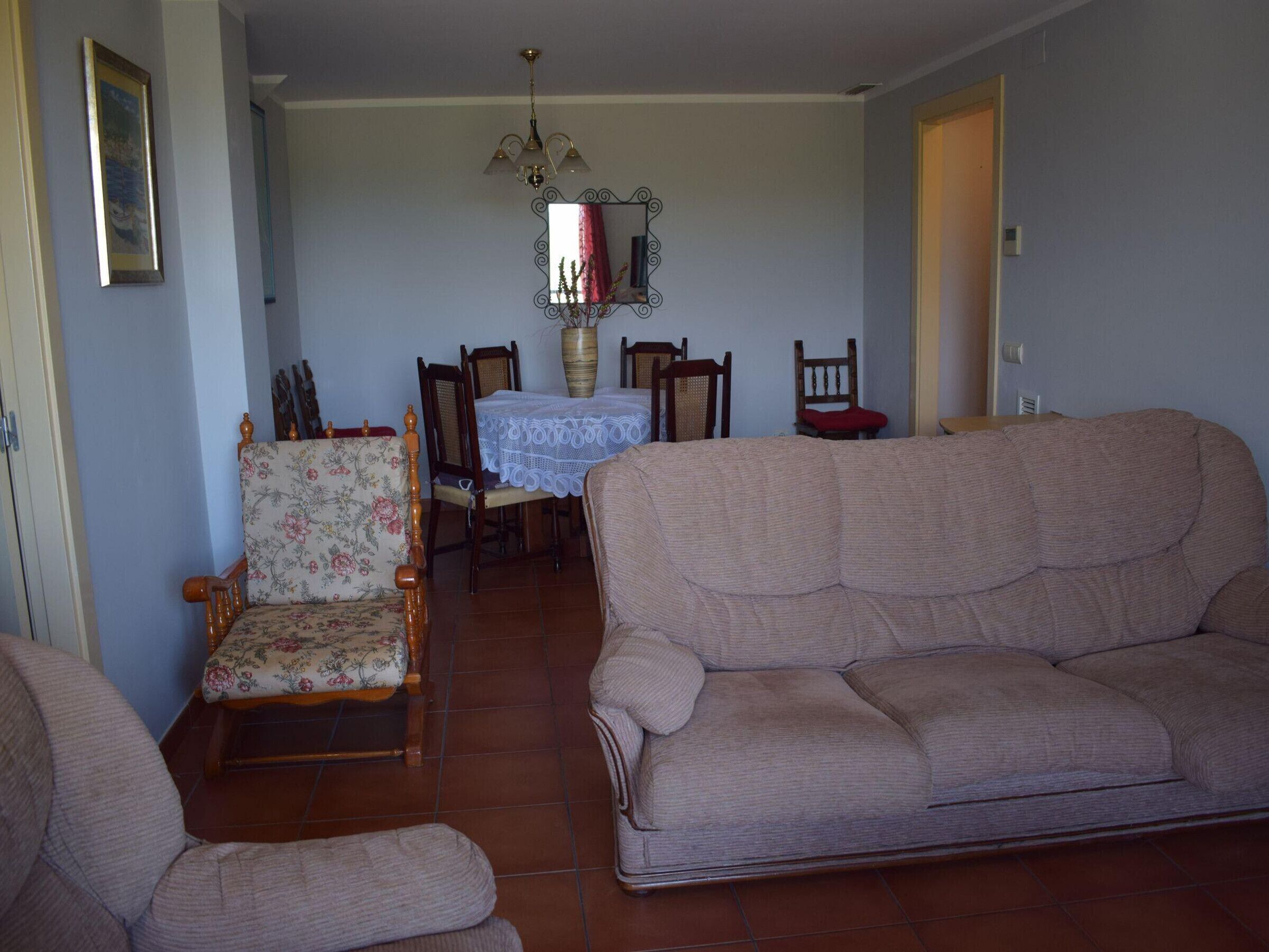 Ein Wohnzimmer mit einem blumigen Sessel, einem beigen Sofa und einem Essbereich mit Tisch und Stühlen.