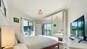 Ein Hotelzimmer mit Bett, Nachttisch, Lampe, Fernseher und einem Balkon mit Blick.