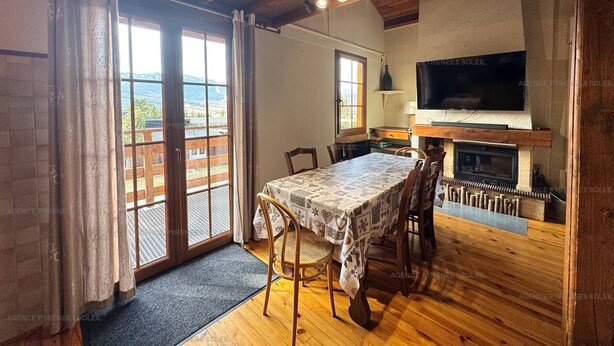 A cozy dining area with a table set for four, a fireplace, and a TV mounted on the wall. - 4-sided Cottage 80m² near lake with garage (Matemale)