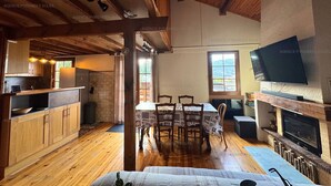 A cozy cabin interior with a wooden dining area, a TV mounted above a fireplace, and a kitchen with wooden cabinets and a built-in oven. - 4-sided Cottage 80m² near lake with garage (Matemale)