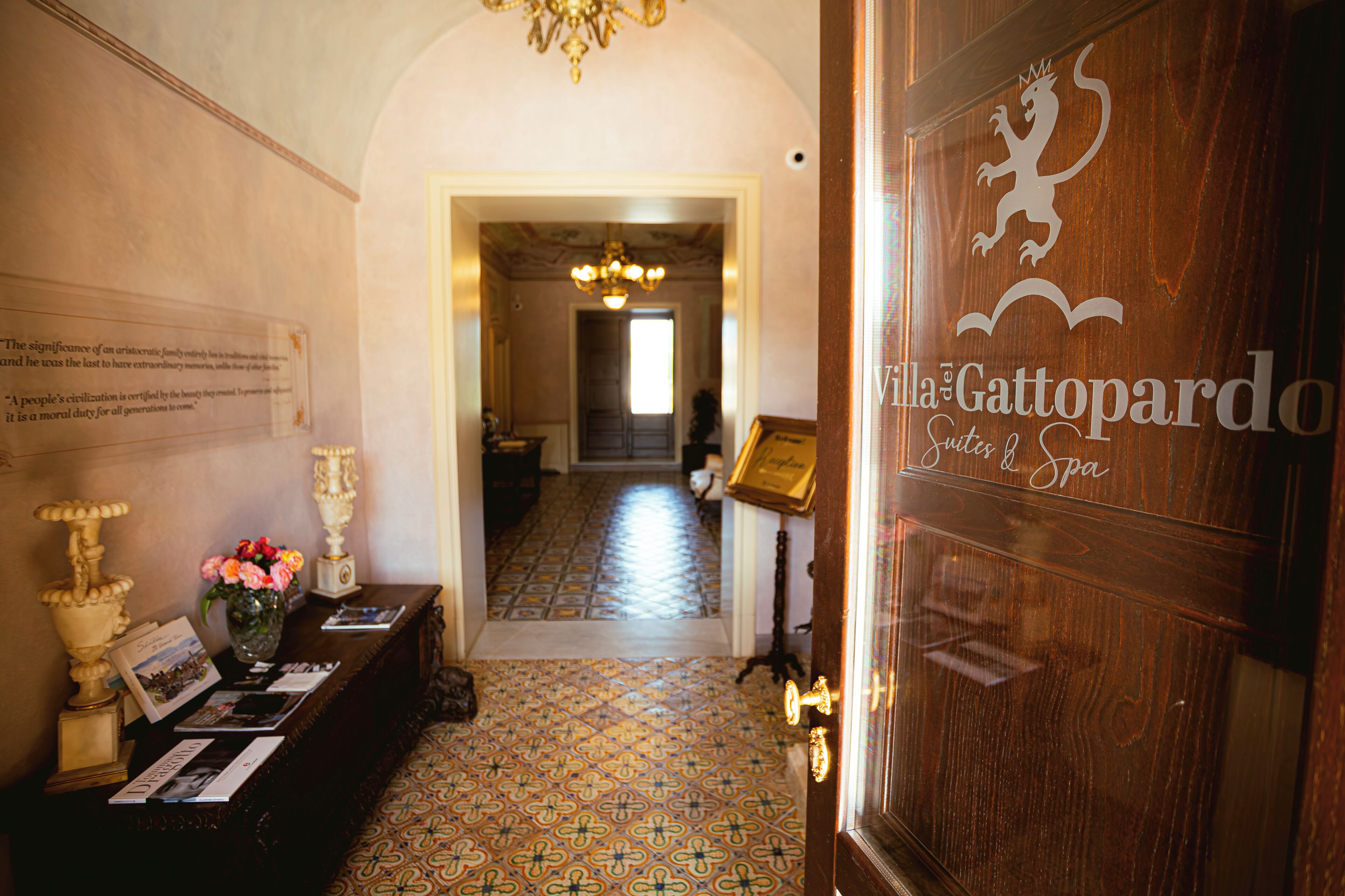 A hallway with patterned flooring, a reception desk with informational brochures, and a door with a coat of arms.
