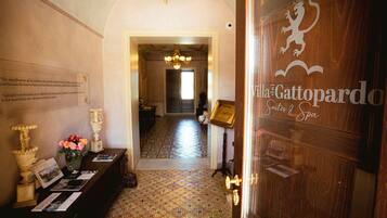 A hallway with patterned flooring, a reception desk with informational brochures, and a door with a coat of arms.