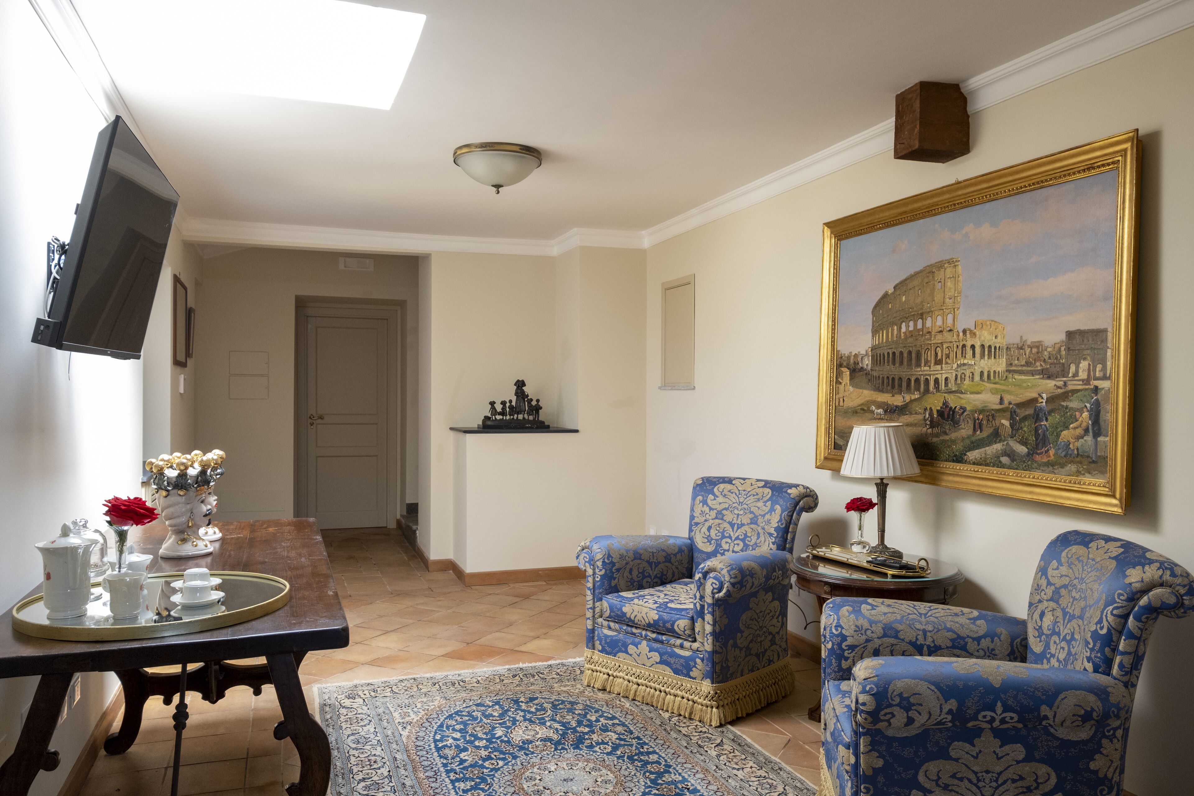 Un soggiorno con una TV, un quadro del Colosseo e due poltrone a fantasia.