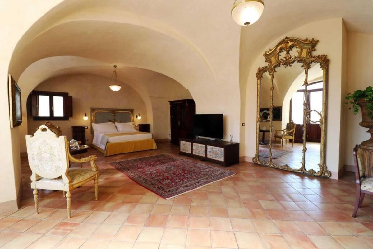 A spacious bedroom with a large bed, a television, and a decorative mirror.