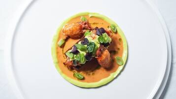 Un plato blanco con un guiso adornado con detalles verdes y púrpuras, y salsa amarilla.
