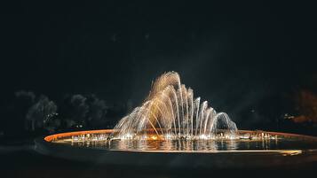 Una fontana illuminata di notte con getti d'acqua, circondata da una piattaforma circolare e uno sfondo scuro.