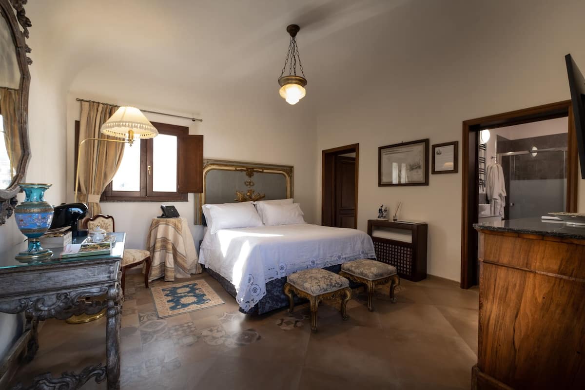A bedroom with a large bed, a desk with a telephone, a chair, a small table with a lamp, and a hanging light fixture.