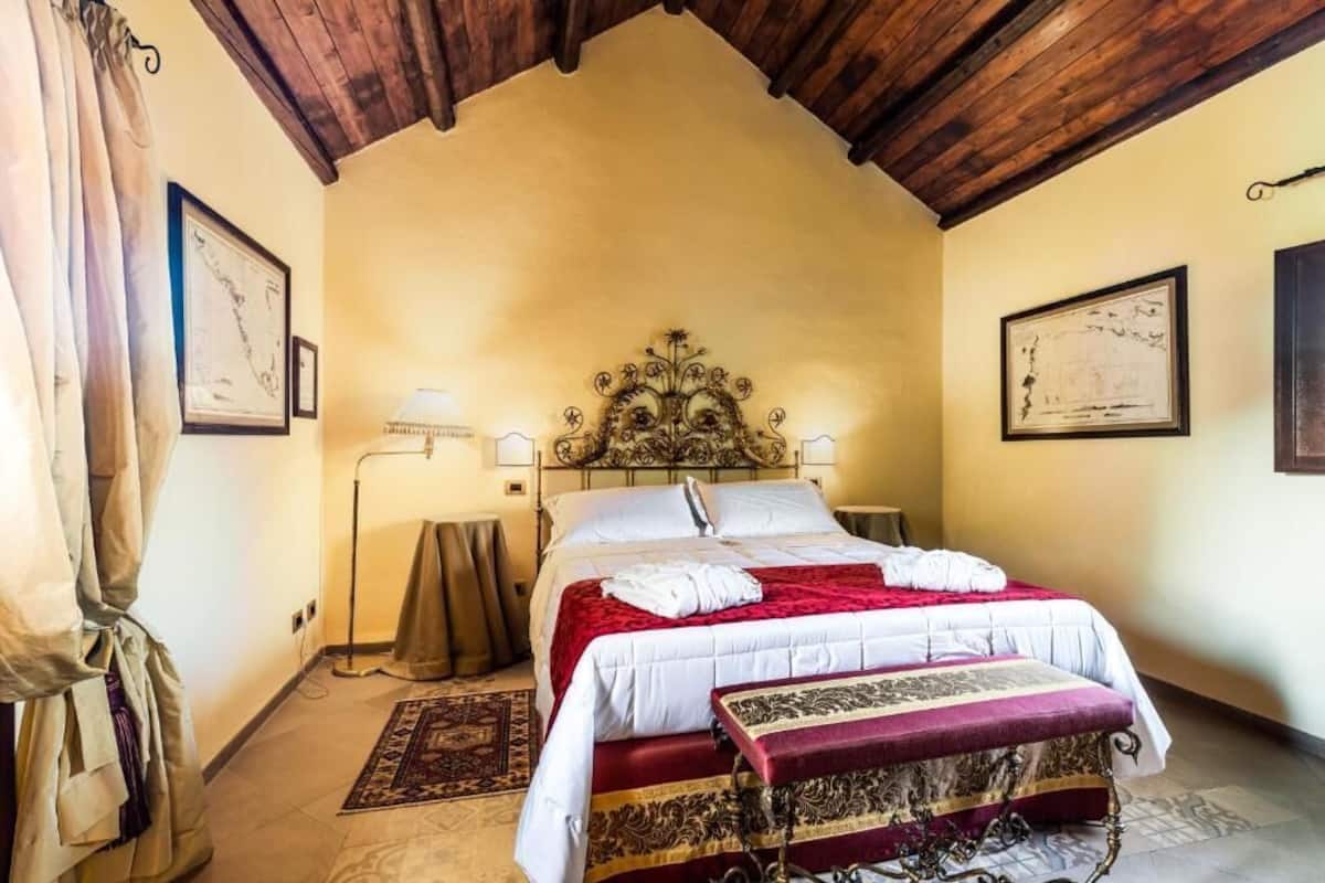 A bedroom with a large bed, a wooden ceiling, and two framed pictures on the walls.