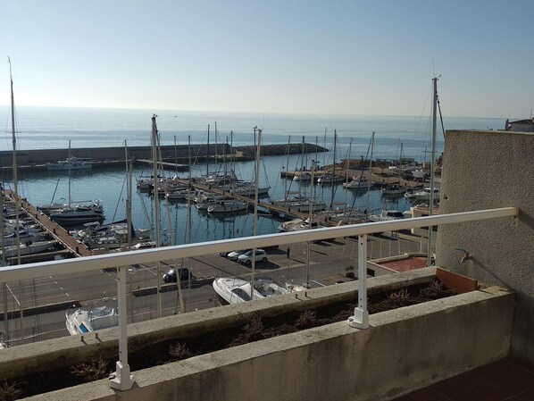 A marina with boats docked, a clear sky, and a view of the sea.