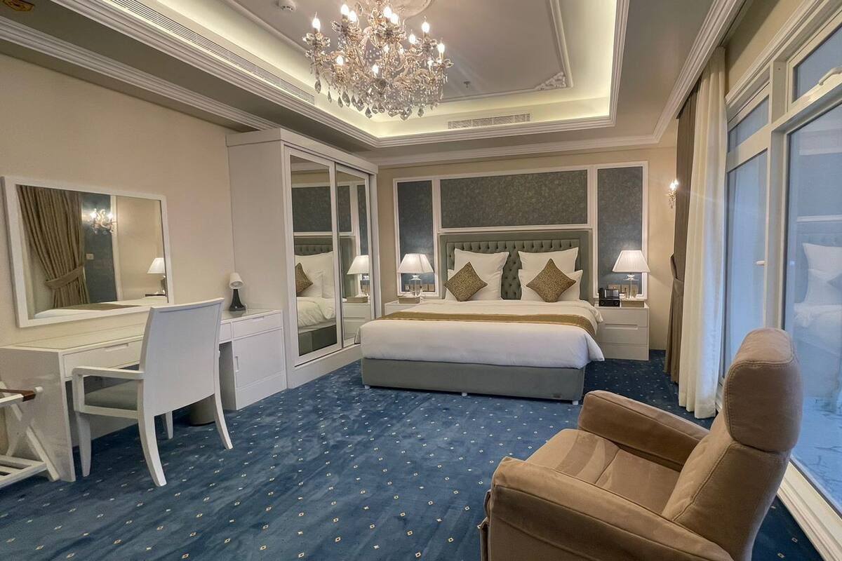 A hotel room with a large bed, a desk, a chair, and a view of the outside.