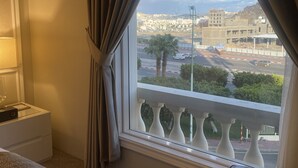 A hotel room with a large window, a bed, a nightstand, and a view of a cityscape. - Remaj Hotel (Taif)