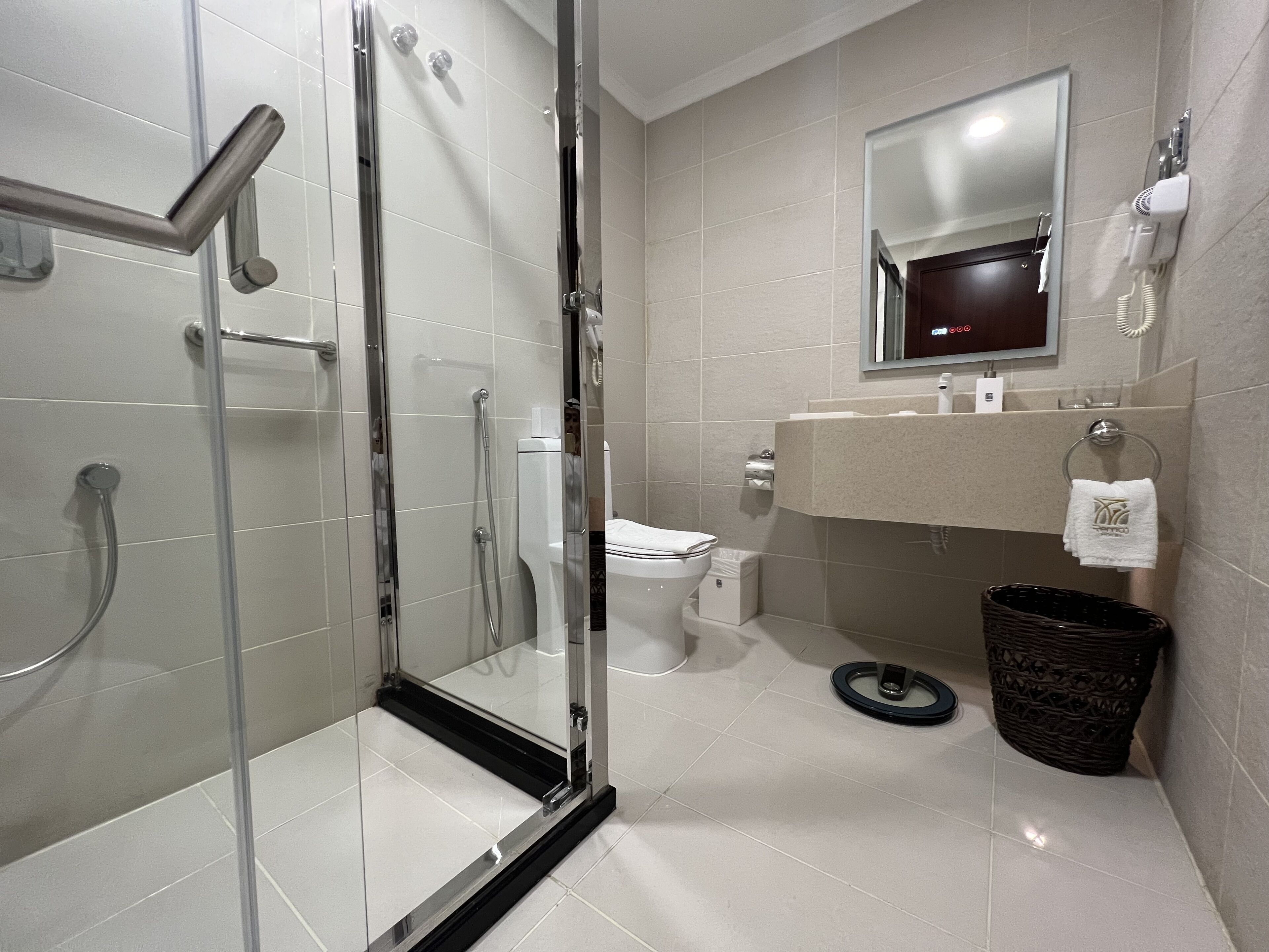Une salle de bain moderne avec une douche à parois de verre, des toilettes, un lavabo avec un porte-serviettes et une poubelle.