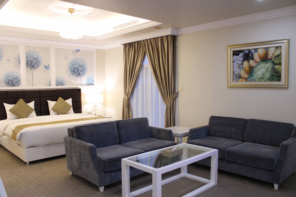 A hotel room with a bed, two sofas, a coffee table, and a painting on the wall.