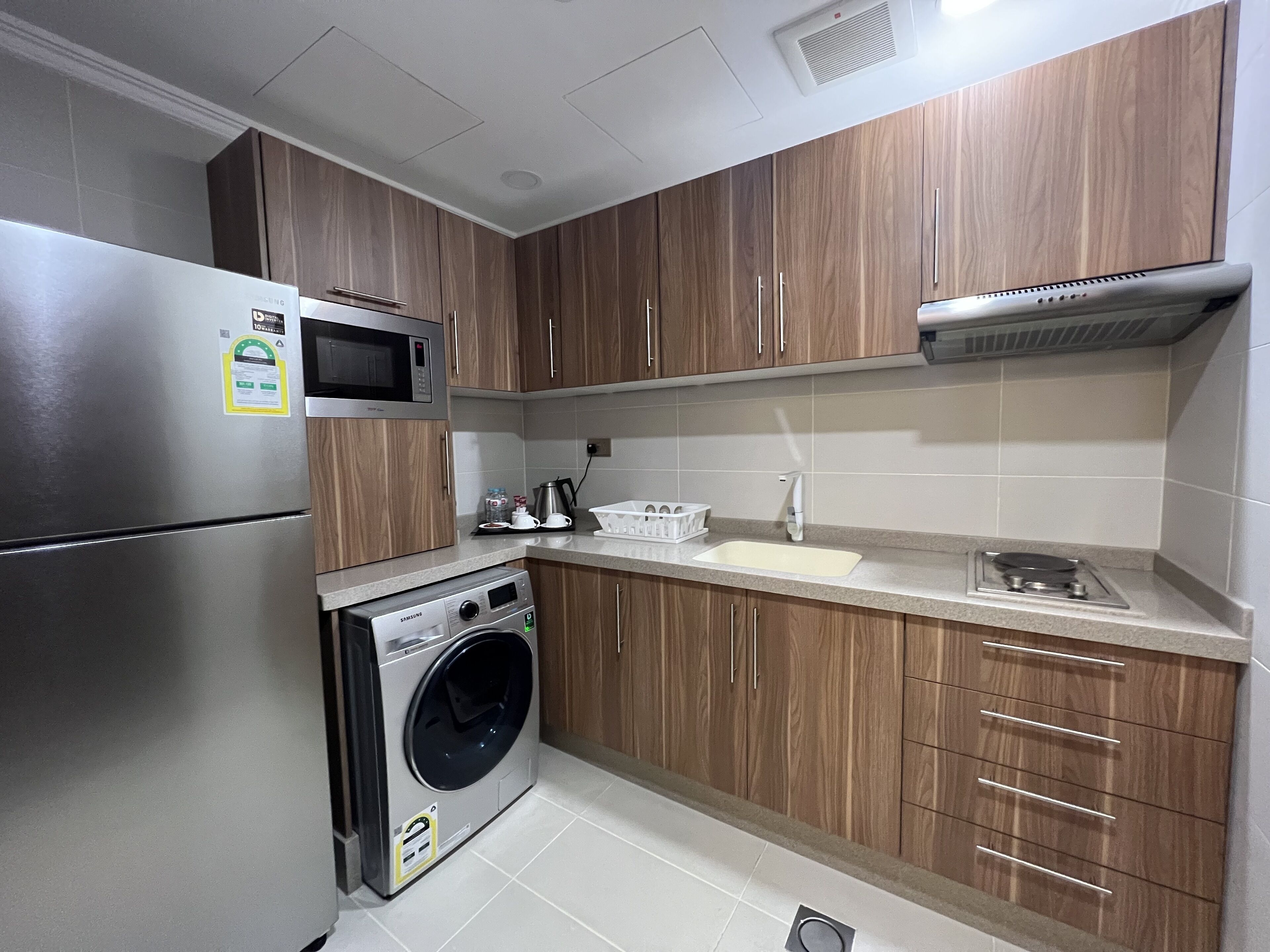 Una cocina compacta con armarios de madera, un refrigerador de acero inoxidable, un microondas, una lavadora y un lavaplatos.