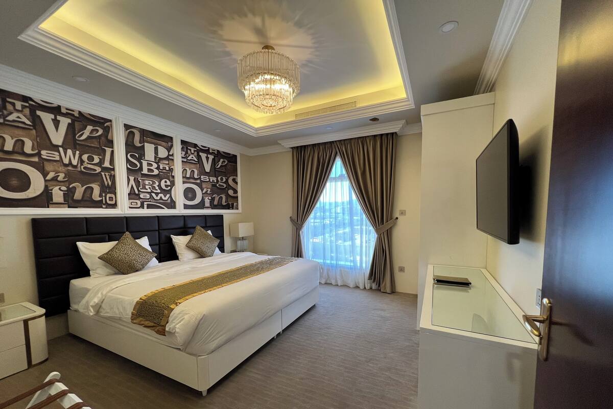A modern hotel room with a large bed, a ceiling light, a TV, and a window with curtains.