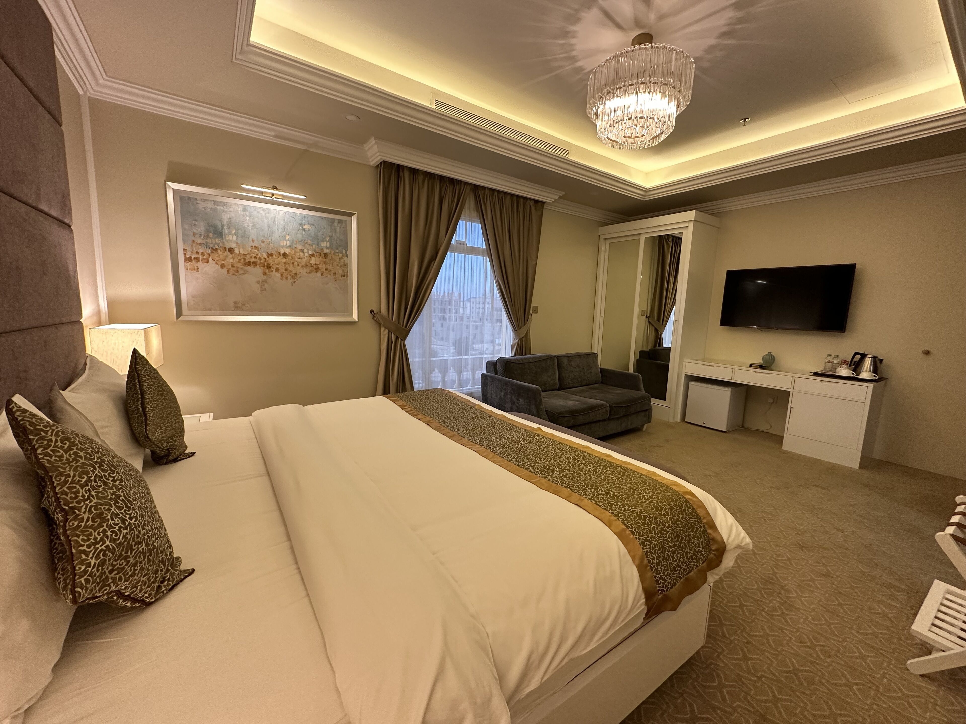 A hotel room with a large bed, a desk, a television, and a view of the city.