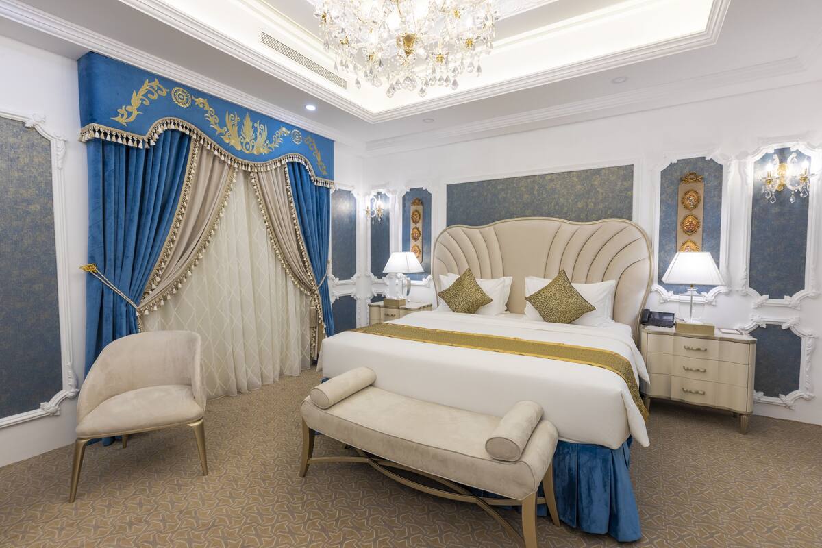 A luxurious bedroom with a large bed, a bench, a chair, and a nightstand with a lamp.