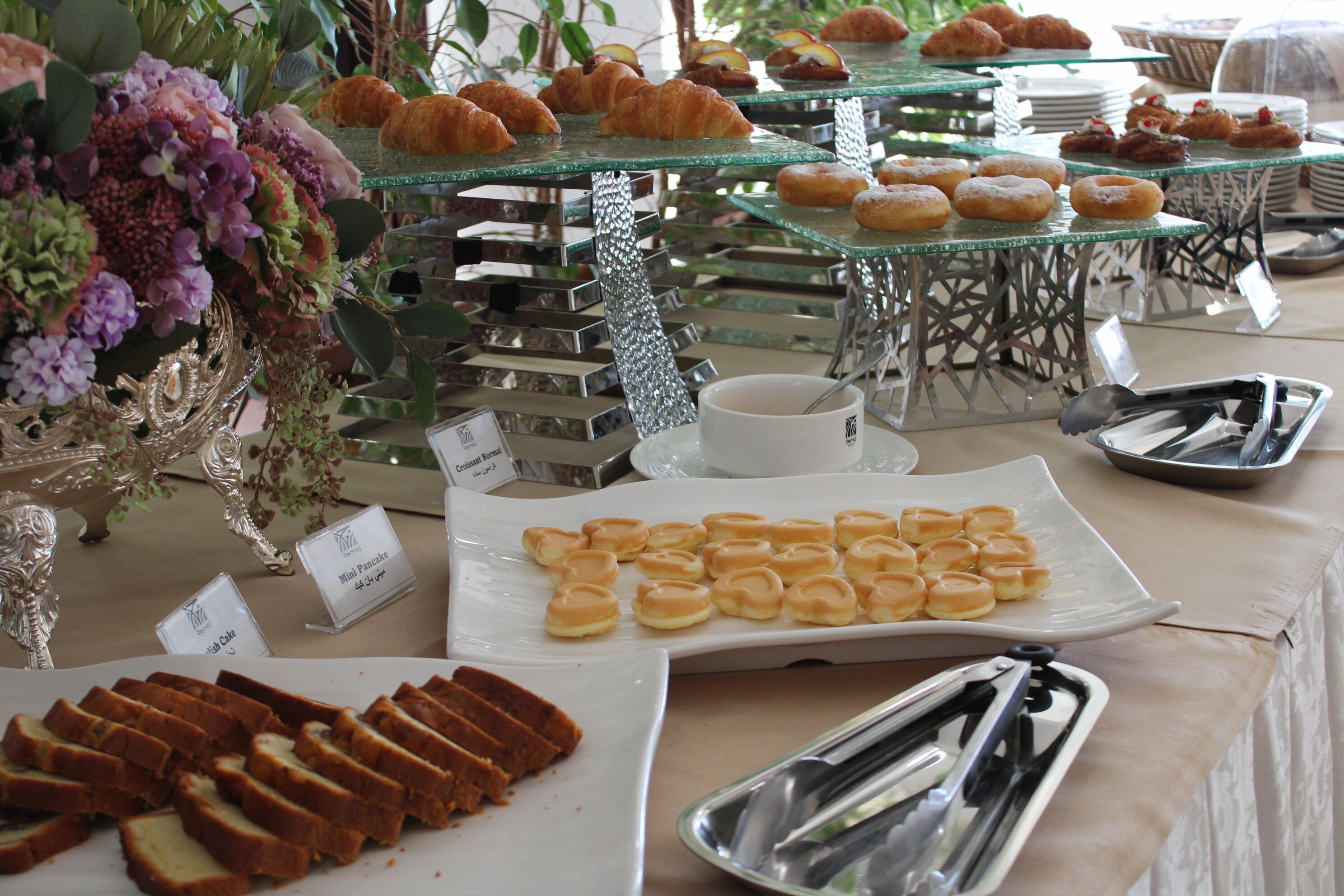 A buffet table with various pastries, including croissants and mini pastries, and a plate of bread slices.