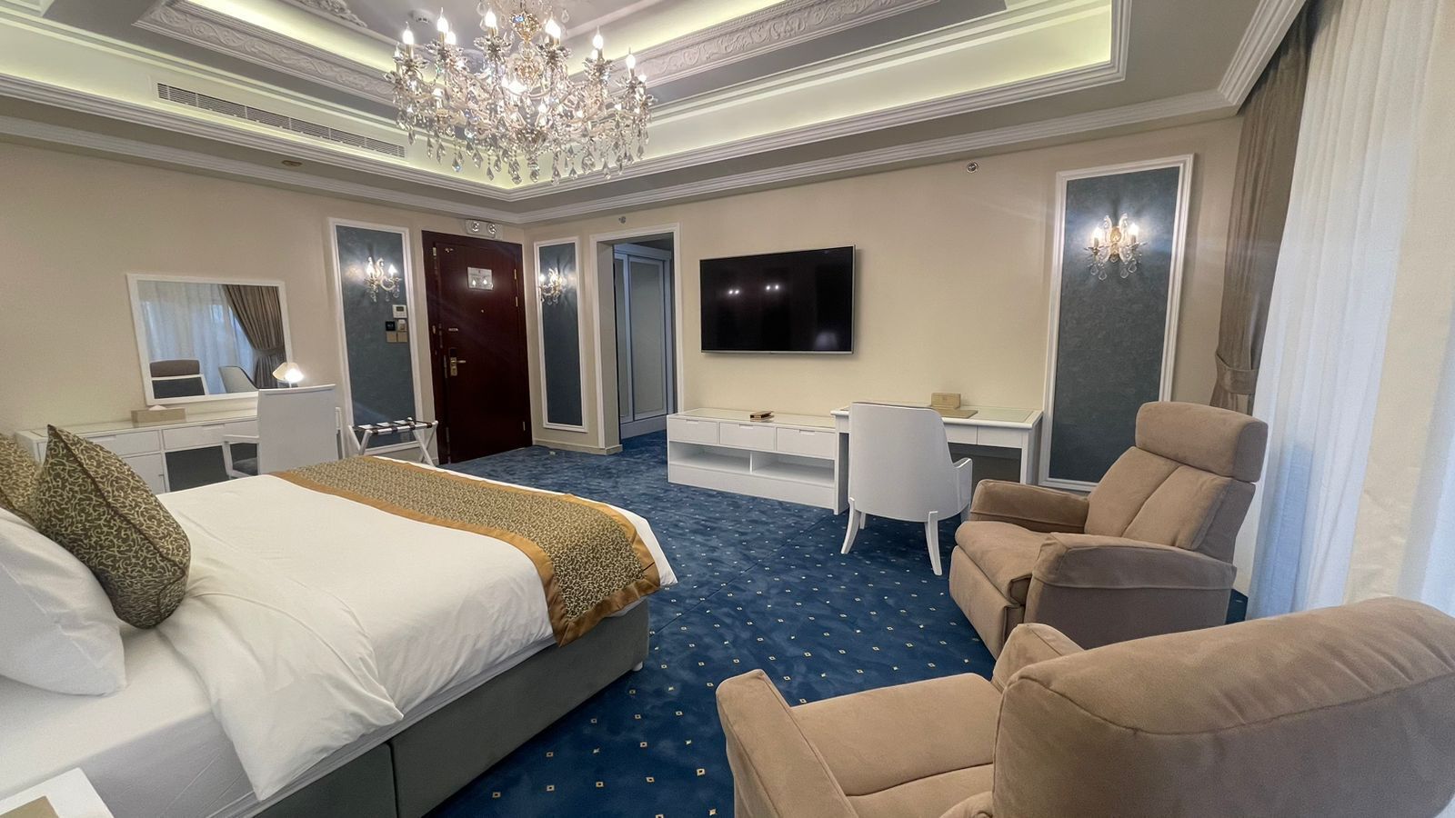 A hotel room with a large bed, a desk, a chair, and a TV.