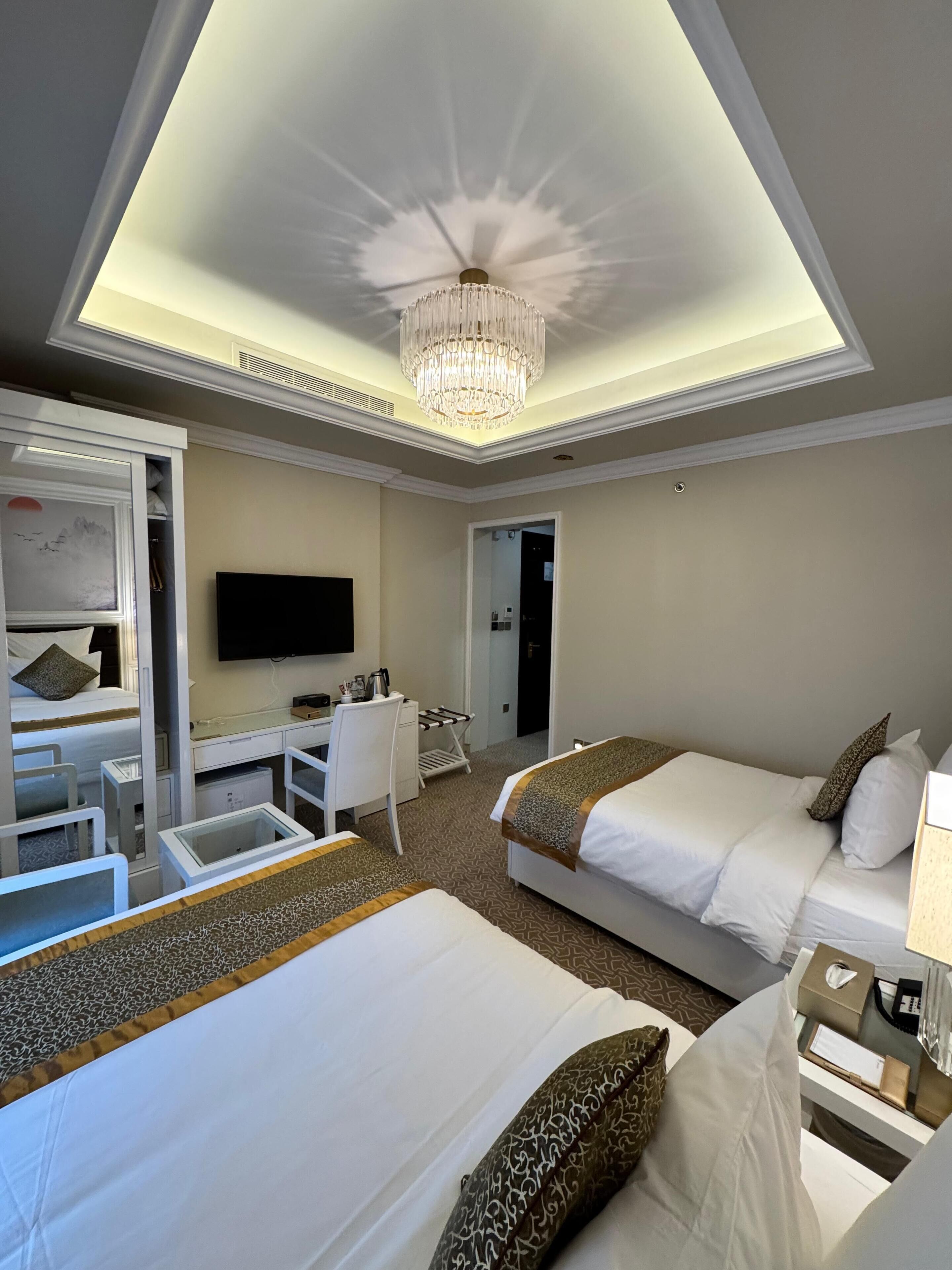 Una camera d'albergo con due letti, una scrivania, una televisione e un lampadario.