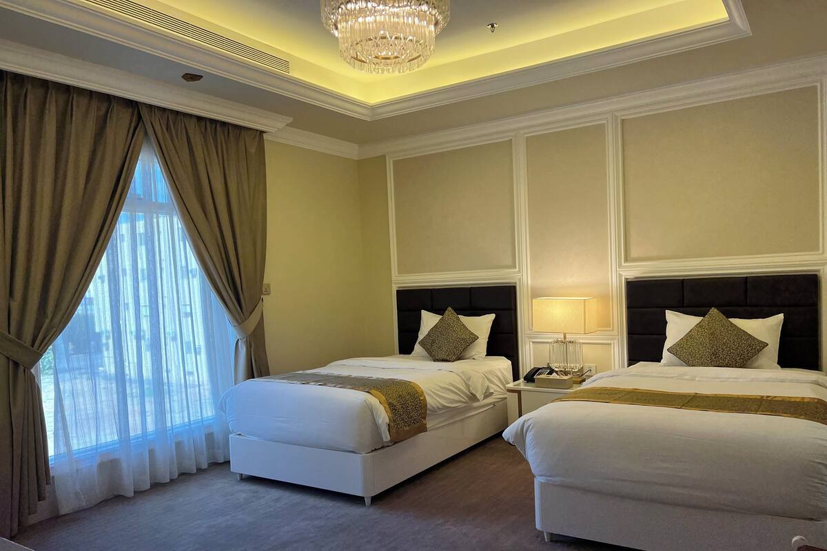 A hotel room with two beds, a chandelier, and a large window with curtains.