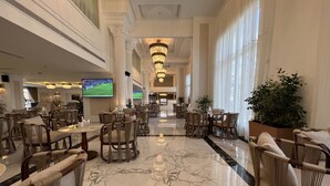 A spacious lobby with marble flooring, multiple seating areas, large windows, and a television displaying a sports event. - Remaj Hotel (Taif)