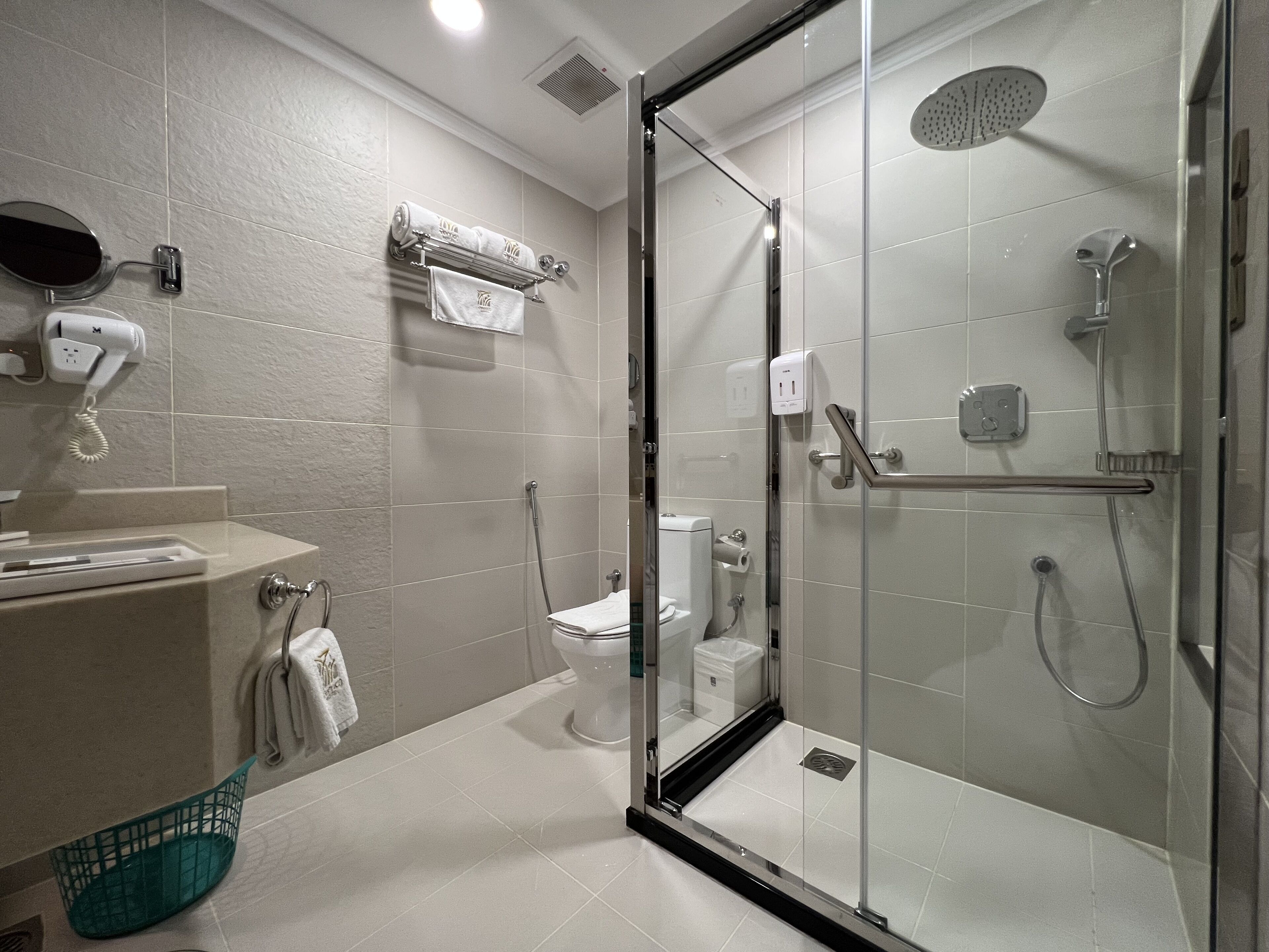 A modern bathroom with a glass-enclosed shower, a toilet, and a sink with a towel rack.