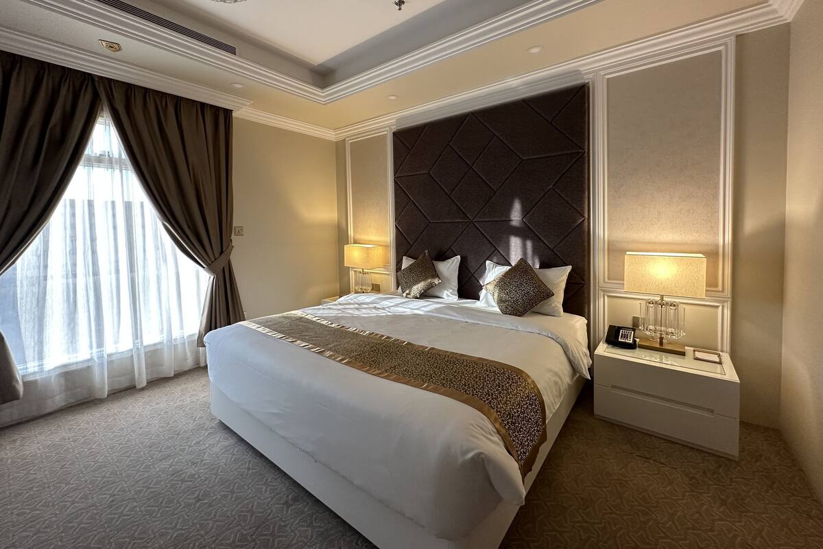 A spacious hotel room with a large bed, two bedside lamps, a nightstand, and a decorative wall panel.