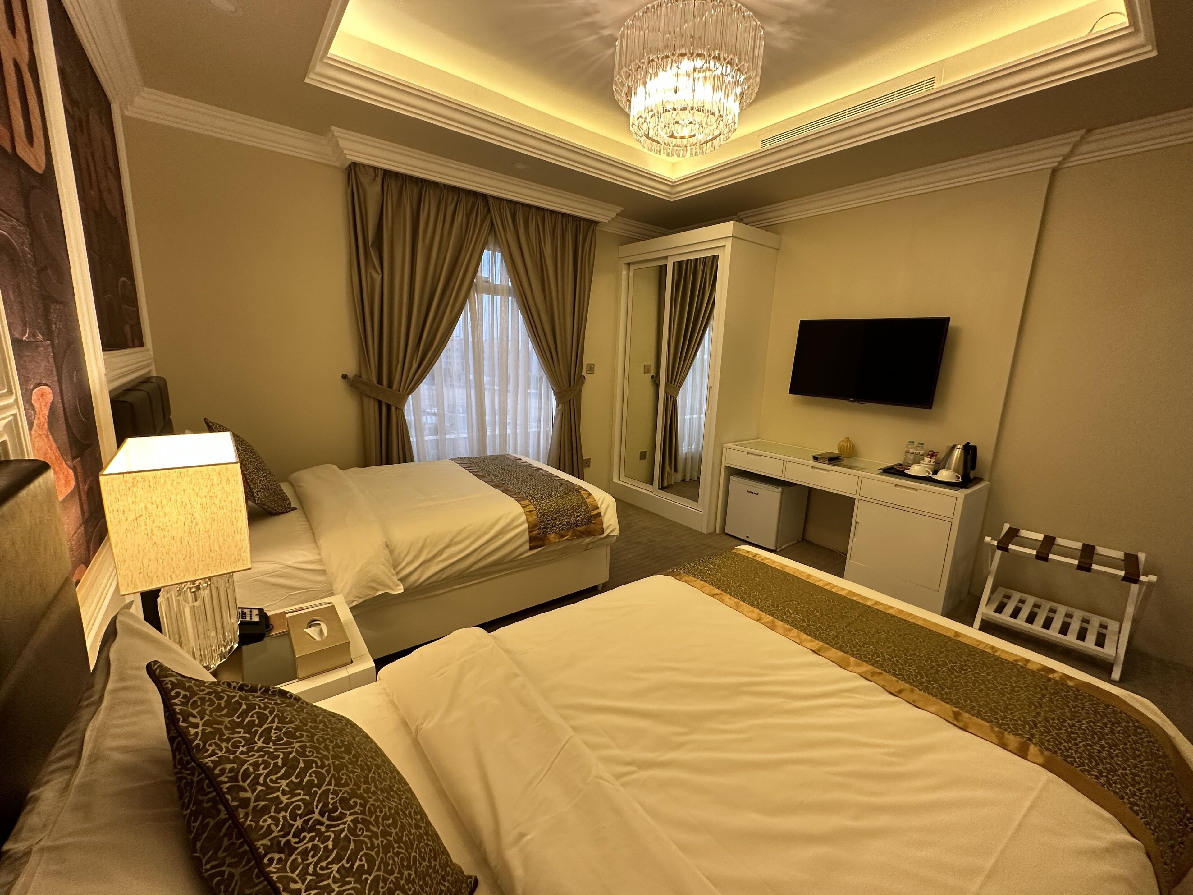 Ein Hotelzimmer mit zwei Betten, einem Schreibtisch, einem Fernseher und einer Chandelier.